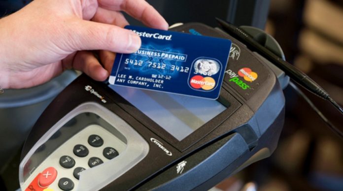 Mano sujetando tarjeta de crédito MasterCard y punto de venta de banco