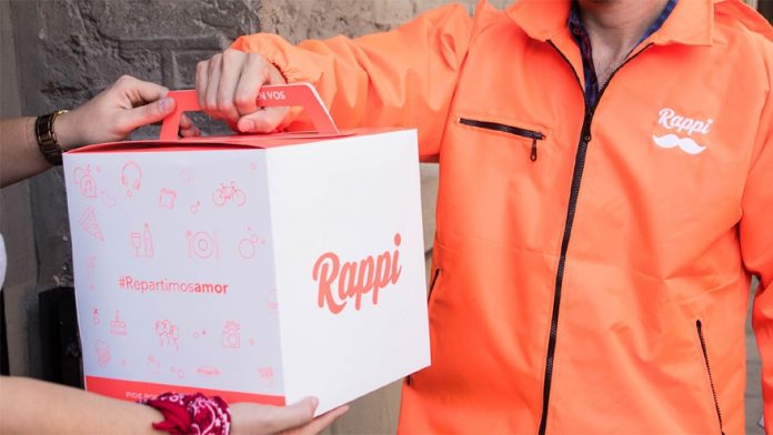 Hombre vestido de naranja entregando caja con publicidad de Rappi