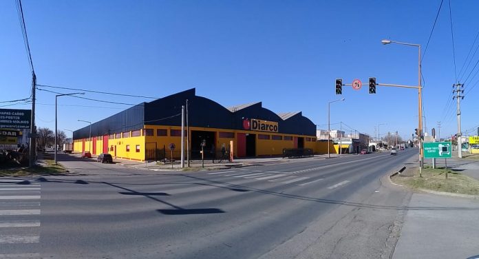 Avenida con galpón amarillo y negro, en la entrada publicidad de Diarco