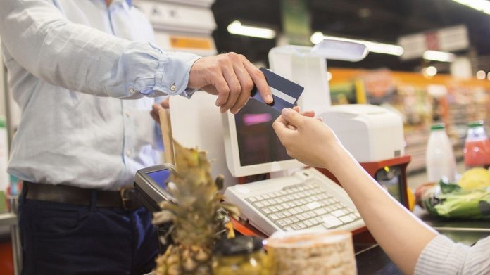 Personas en automercado con tarjeta de banco en manos y caja registradora