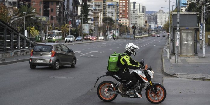Avenida con carros, edificios, hombre en moto llevando delivery