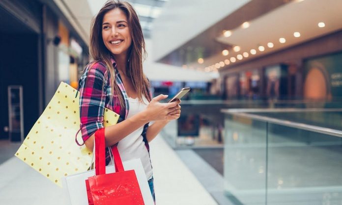 Mujer con celular en la mano y bolsas de compras