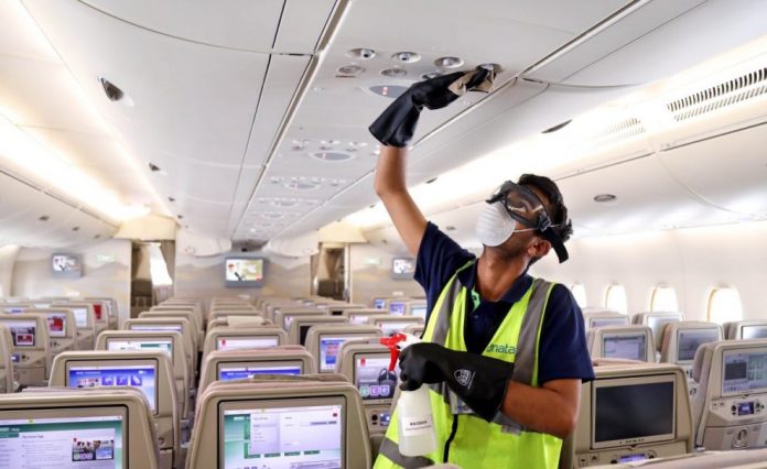 Interior de un avión, hombre con chaleco, tapabocas y lentes haciendo mantenimiento