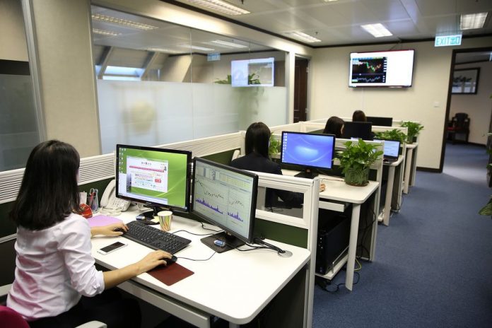 Oficina con ventanas de vidrio, lámparas, escritorios blancos, computadoras, plantas decorativas y mujeres trabajando