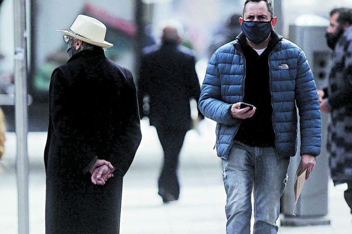 Hombre con sobretodo negro y sombrero blanco, hombre con chaqueta azul y celular en la mano