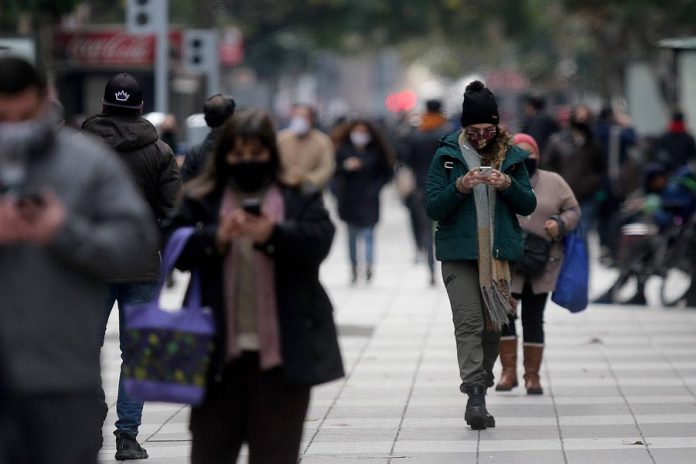 Avenida, personas con tapabocas caminando con celulares en las manos