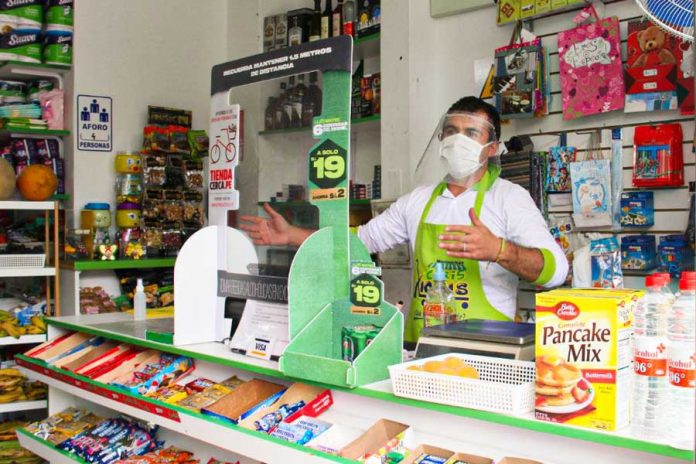 Tienda con anaqueles de diferentes productos, hombre con delantal verde, tapaboca blanco, máscara facial atendiendo