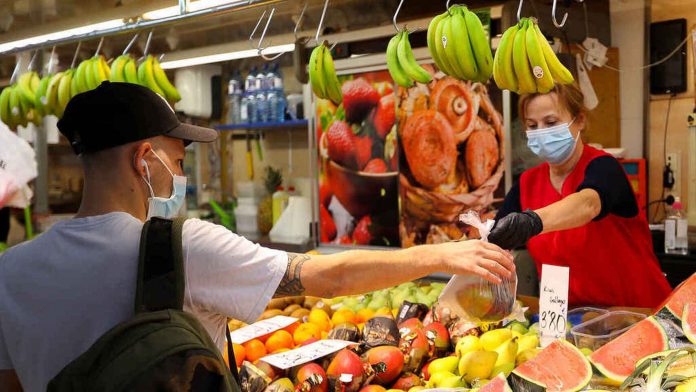 Supermercado, anaqueles con productos y frutas, mujer atendiendo, hombre comprando, ambos con tapabocas