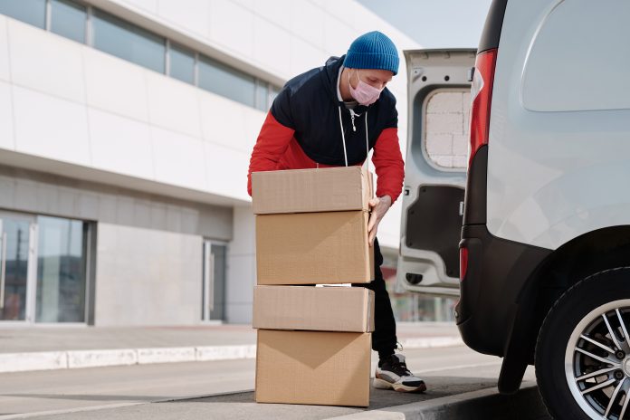 Trabajador de empresas minoristas de delivery cargando cajas sobre el maletero de un carro.