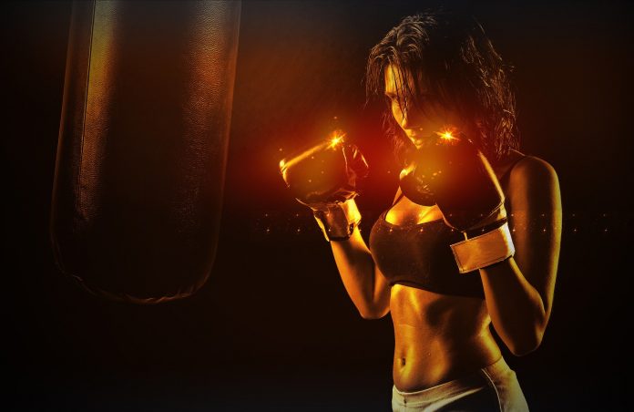 Mujer en ropa deportiva con guantes de boxeo practicando ejercicio en un cuchimbolo