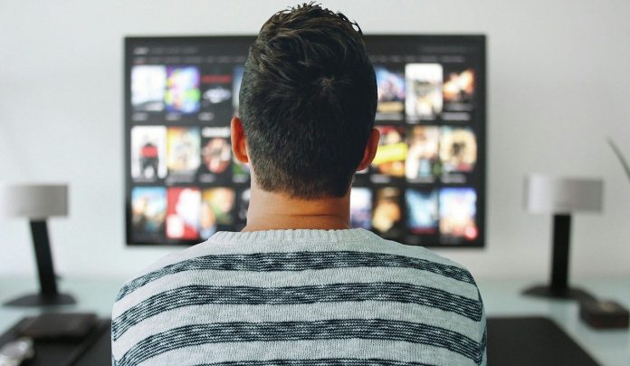 Hombre de espalda con franela de raya, pantalla de televisión mostrando aplicaciones