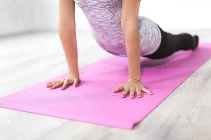 Mujer practicando yoga en alfombra rosada