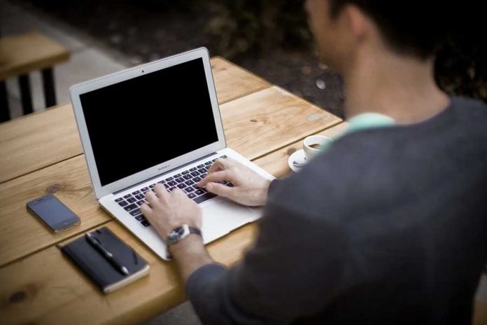 Mesa de madera, persona tecleando laptop, celular, agenda, bolígrafo y taza de café