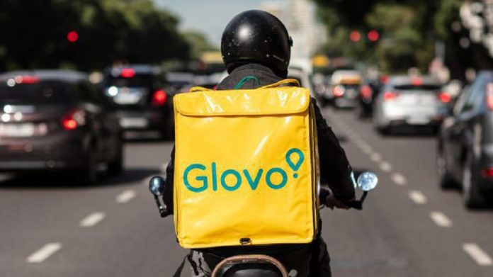 Autopista, hombre con casco en moto y maleta de entrega con publicidad glovo