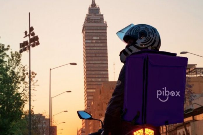 Edificaciones, hombre en moto con casco y maleta de entrega con publicidad pibox