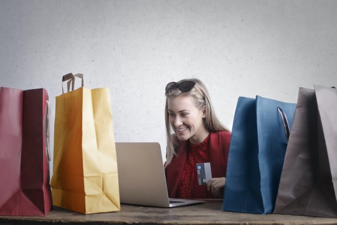 Mujer con laptop, tarjeta de banco en las manos y bolsas de colores a los lados