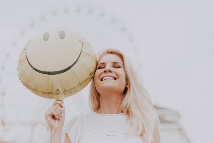 Mujer vestida de blanco, sonriendo y sosteniendo globo de carita feliz