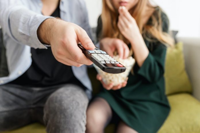 Personas sentadas en sofá, comiendo pop corn con control de televisor en las manos. Totalplay