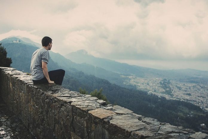 Hombre sentado en un muro de piedras viendo el horizonte