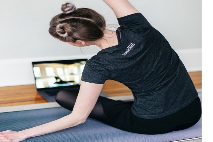 Mujer con ropa deportiva frente a una laptop haciendo ejercicios