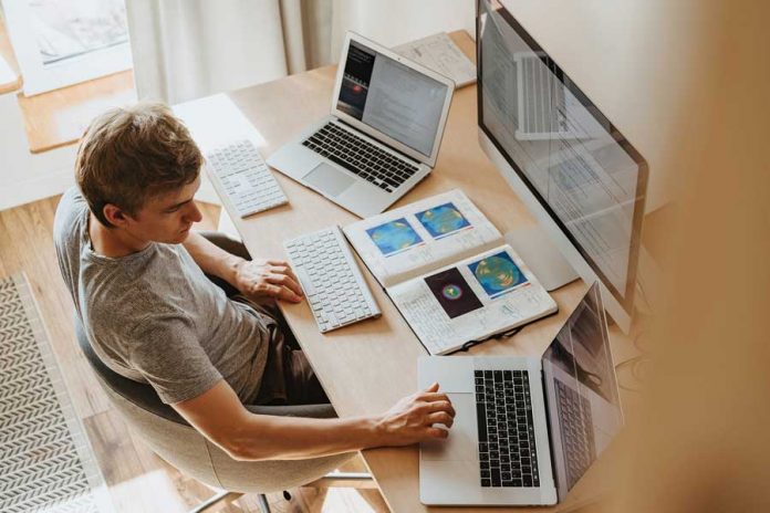 Hombre en habitación, mesa con laptops, pantalla de computadora y libro