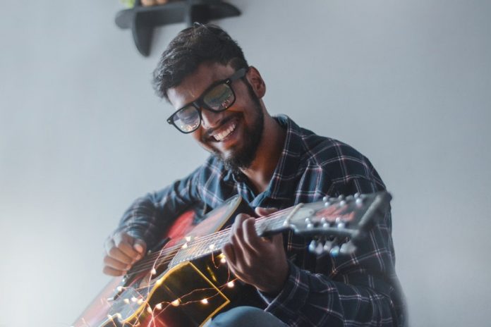 Hombre de lente y camisa de cuadros tocando guitarra