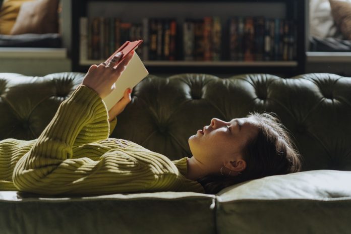 Mujer acostada en sofá leyendo un libro