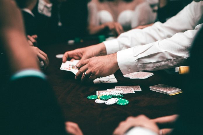 Mesa con barajas de poker y monedas de juego, manos con barajas