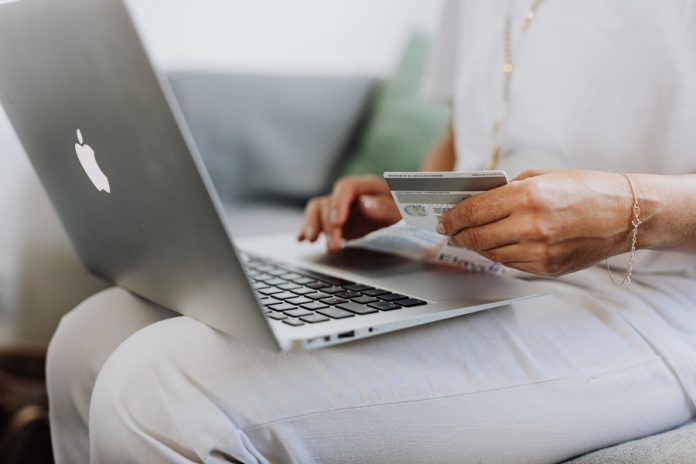 Mujer sentado con laptop y tarjeta de débito en las manos
