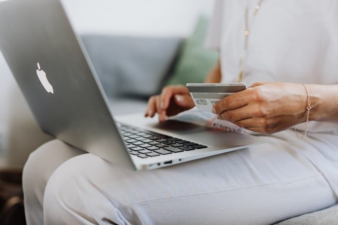 Mujer sentada con laptop y tarjeta de banco en las manos