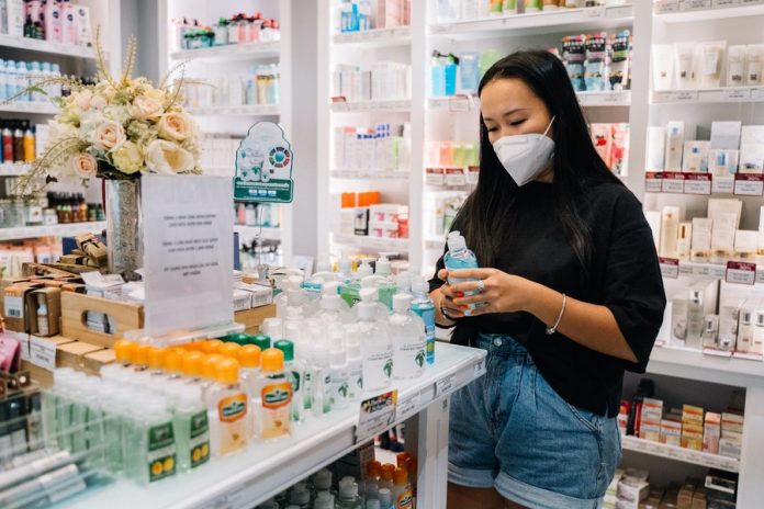 Interior de farmacia, anaquel con productos, mujer observando y con frasco en las manos