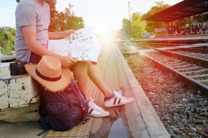 Persona sentado con maleta, mapa, sombrero, esperando un tren