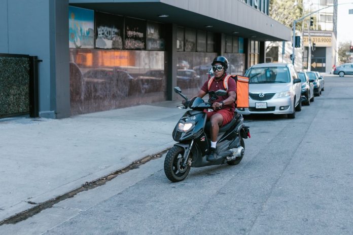 Avenida con locales, persona en moto con maleta de delivery