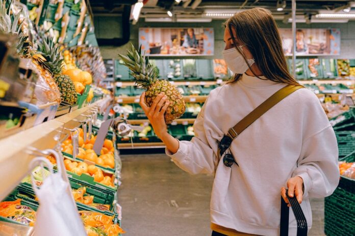 Interior de supermercado, estantería con productos, mujer con frutas en las manos