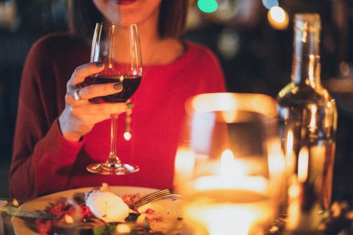 Interior de restaurante, mesa con plato de comida, mujer con copa de vino