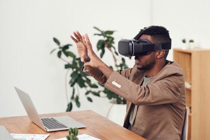 Interior de oficina, escritorio con laptop, hombre con lentes de realidad virtual