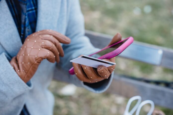 Mujer con guantes marrones, celular y tarjeta de banco en las manos
