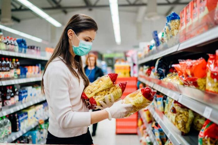 Mujer tomando tres paquetes de pasta en el stand de un supermercado. Estadounidenses, consumo masivo