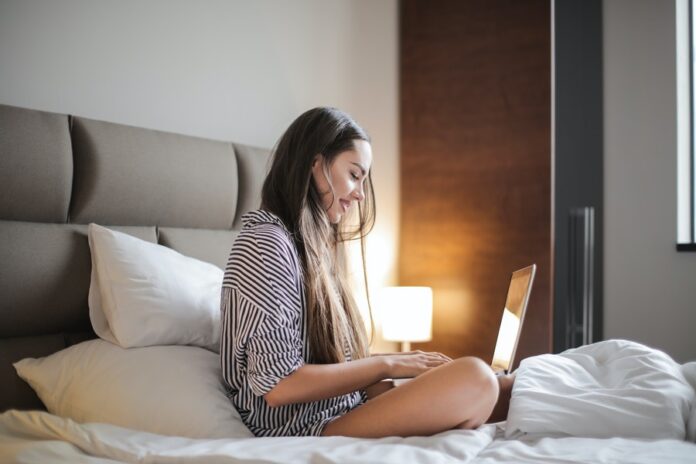 Mujer joven sentada en su cama con una laptop. Streaming