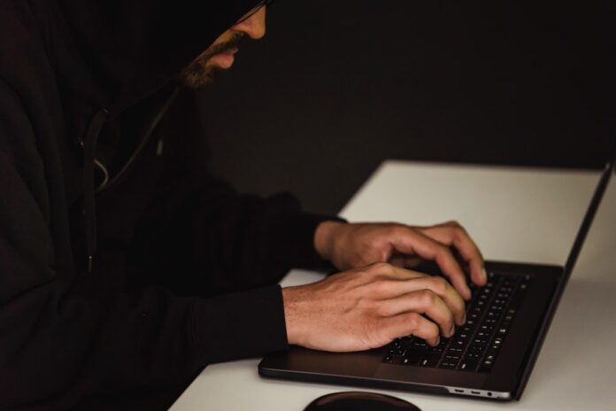 Hombre con suéter de capucha negra trabajando con laptop
