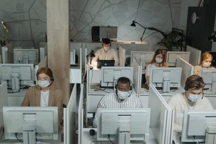 Interior de oficina compartida, personas trabajando con computadora y audífonos