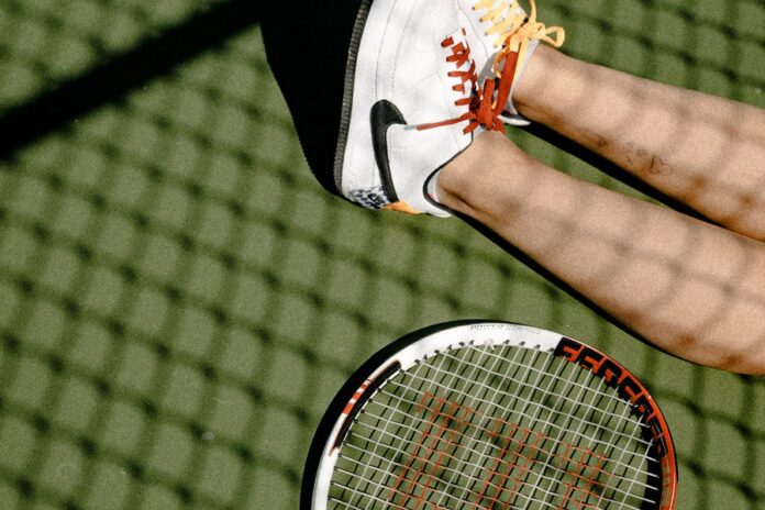 Persona sentada en el piso con las piernas estiradas y raqueta de tenis
