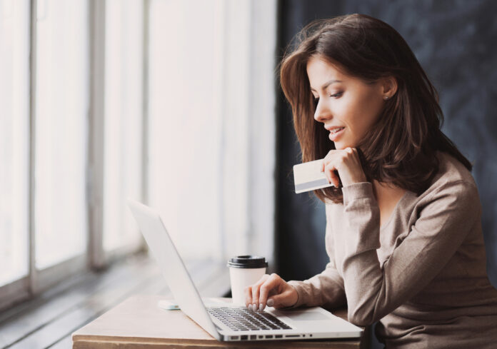 Mujer trabajando con laptop, vaso de café y tarjeta de banco en las manos