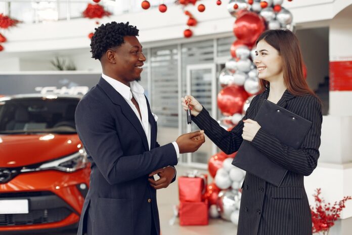 Mujer entregando llave a un hombre, interior de concesionario, vehículo rojo