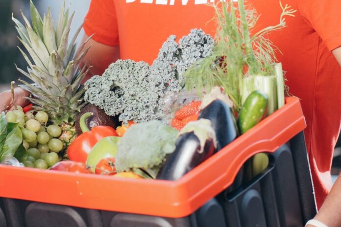 Trabajador de delivery entrega una caja de mercado con frutas, verduras y hortalizas. La Comer