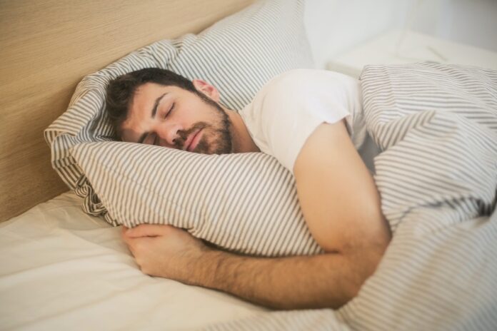 Hombre con una franela blanca durmiendo abrazado a su almohada