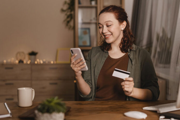 Mujer sonriendo usando un smartphone con una tarjeta de crédito